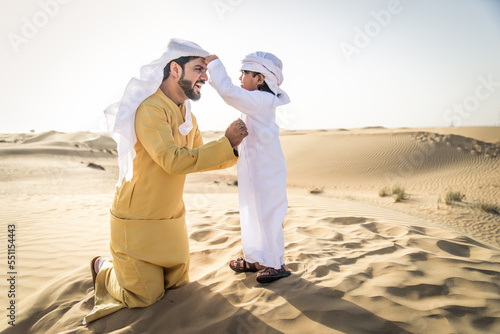 Playful arab man and his son wering traditional middle eastern emirate clothing playing and having fun in the desert of Dubai