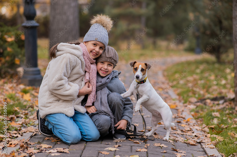 Caucasian boy and girl posing sitting on sidewalk with jack russell terrier dog in park in autumn. Caucasian boy and girl posing sitting on sidewalk with jack russell terrier dog in park in autumn.