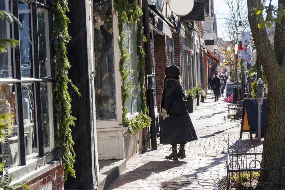 Woman in winter clothing standing on a sidewalk looking into a store window