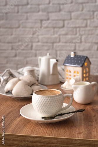 Winter composition on a wooden background. A cup of coffee, white glazed cookies, a creamer, a coffee pot and a decorative house on a wooden table. Cozy winter concept. Selective focus.