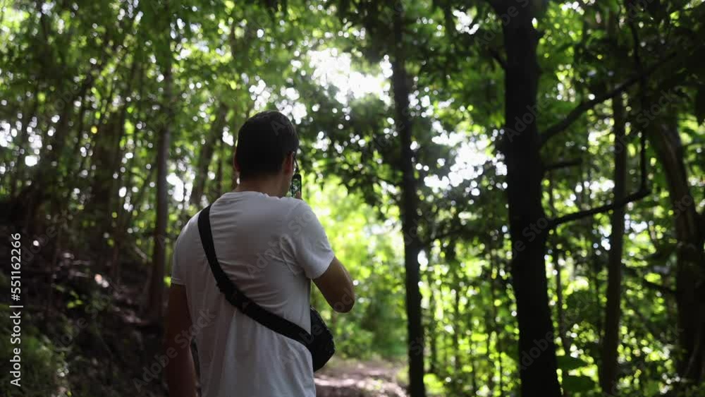 A man using a mobile phone to take pictures of a green forest on a hike A man using a mobile phone to take pictures of a green forest on a hike