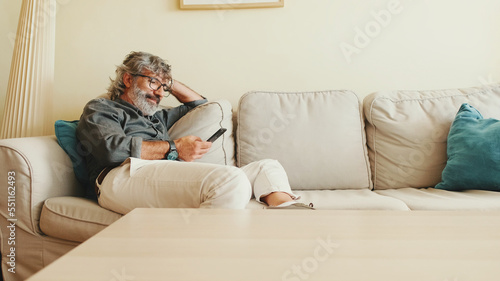 Middle-aged man relaxing on his couch while in home and using his smartphone to text