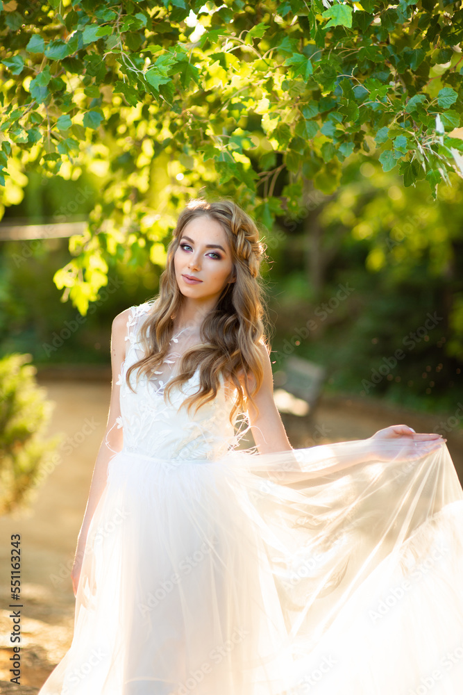 beautiful woman bride in a white wedding dress in the garden in the rays of the setting sun