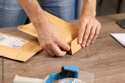 Post office worker sealing adhesive paper bag at counter indoors, closeup