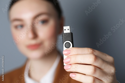 Vászonkép Woman holding usb flash drive against grey background, focus on hand