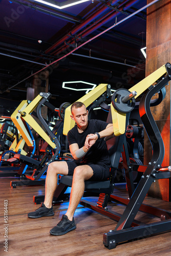 A young man in shorts and a T-shirt is sitting on an exercise machine in a gym. Healthy Lifestyle