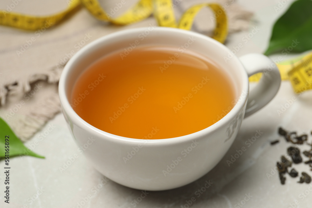 Cup of herbal diet tea and measuring tape on light marble table, closeup. Weight loss concept Cup of herbal diet tea and measuring tape on light marble table, closeup. Weight loss concept