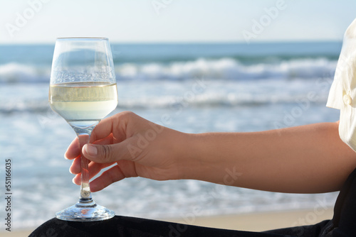 Woman with glass of tasty wine near sea, closeup