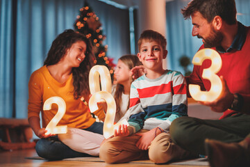 Parents and children holding illuminative numbers 2023 while celebrating New Year