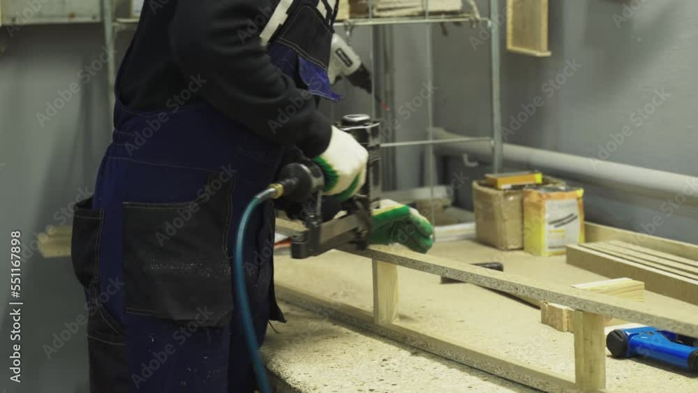 Close-up of a man's hand holding a pneumatic stapler and attaching wood pieces. Furniture manufacturing. Close-up of a man's hand holding a pneumatic stapler and attaching wood pieces. Furniture manufacturing.