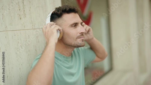 Young hispanic man listening to music and dancing at street