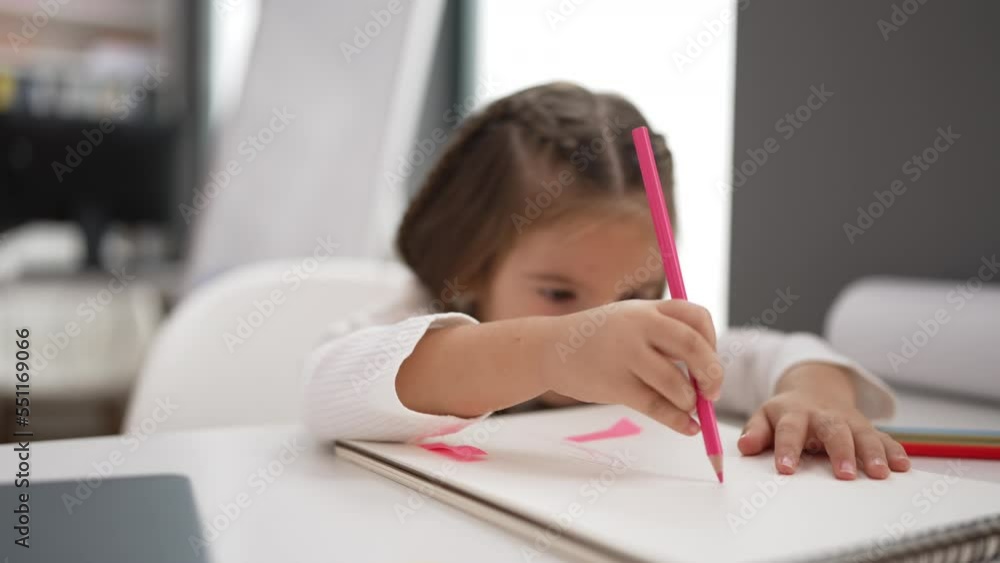 Adorable hispanic girl student sitting on table drawing on paper at kindergarten Adorable hispanic girl student sitting on table drawing on paper at kindergarten