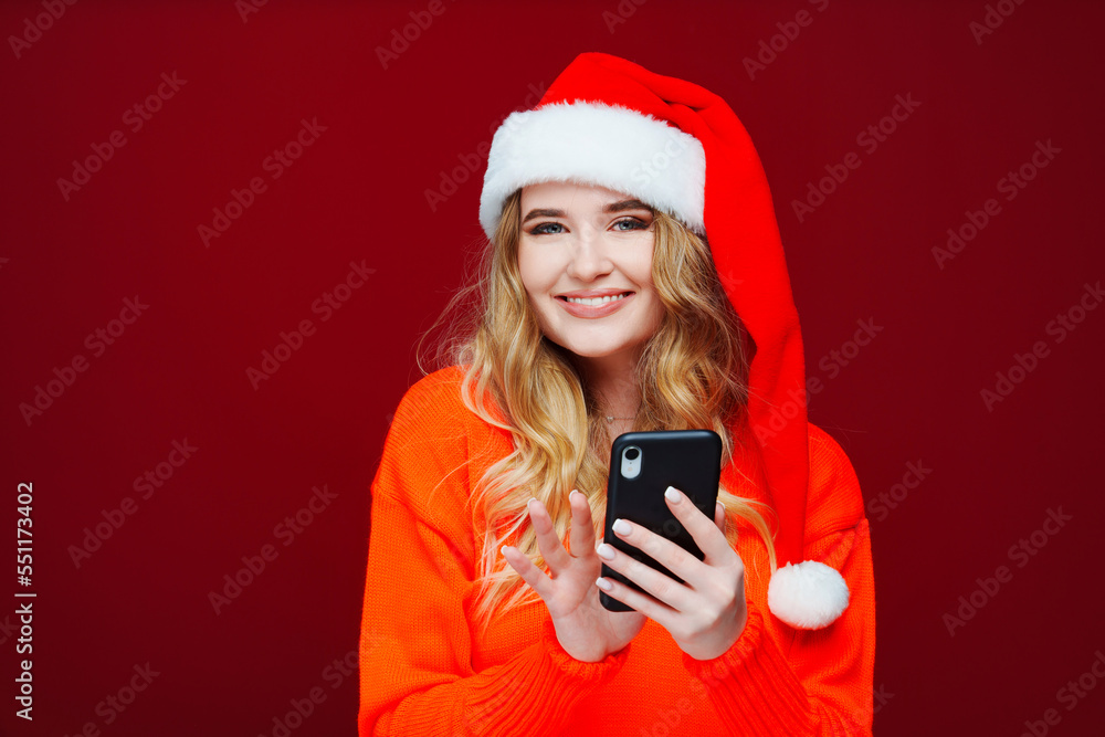 a beautiful woman in a Santa Claus hat with smartphone on a red background. a beautiful woman in a Santa Claus hat with smartphone on a red background.