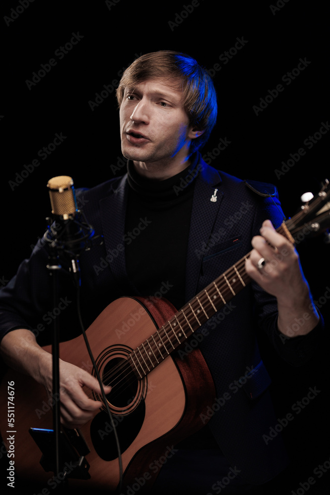 Obraz premium Male musician with guitar in hands playing and posing on black background in blue scenic light