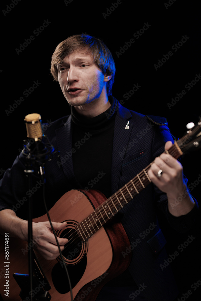 Male musician with guitar in hands playing and posing on black background in blue scenic light