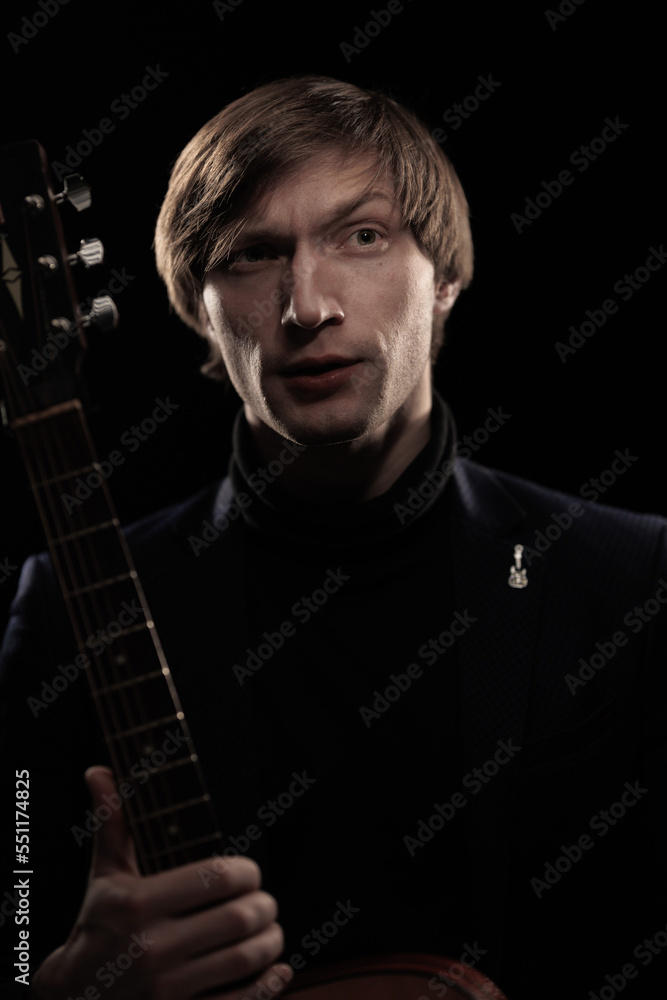 Obraz premium Male musician with guitar in hands playing and posing on black background in blue scenic light