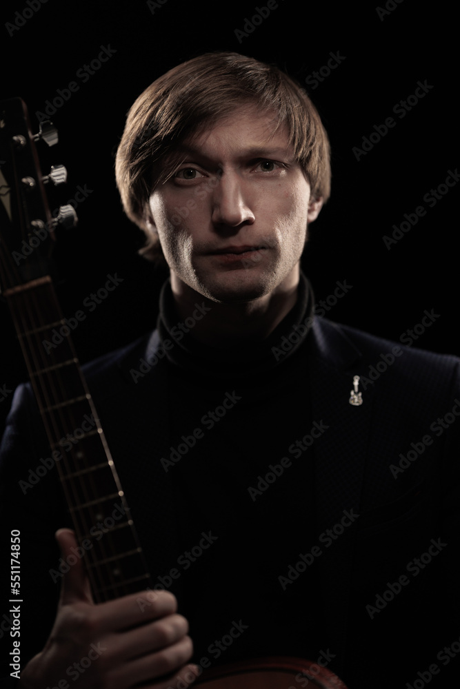 Obraz premium Male musician with guitar in hands playing and posing on black background in blue scenic light
