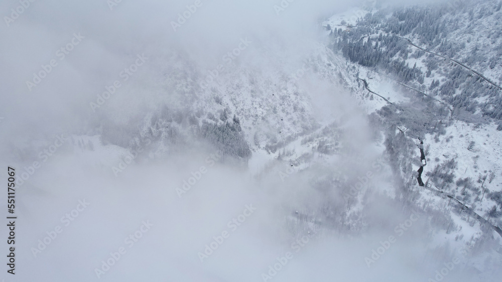 Snowy mountains with coniferous trees in the clouds. Medeo Dam. Everything is in fog and snow. Christmas and New Year have come. Aerial view from the drone on road, dam and trees. Almaty, Kazakhstan