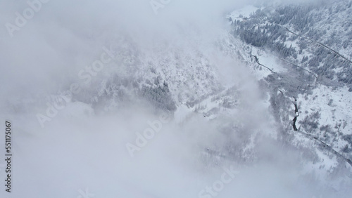 Snowy mountains with coniferous trees in the clouds. Medeo Dam. Everything is in fog and snow. Christmas and New Year have come. Aerial view from the drone on road, dam and trees. Almaty, Kazakhstan © SergeyPanikhin