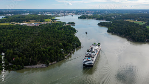 Luxury cruise vessel making way ahead in beautiful Finnish archipelago. Narrow fairway and shoreline proximity. High altitude aerial stern view.