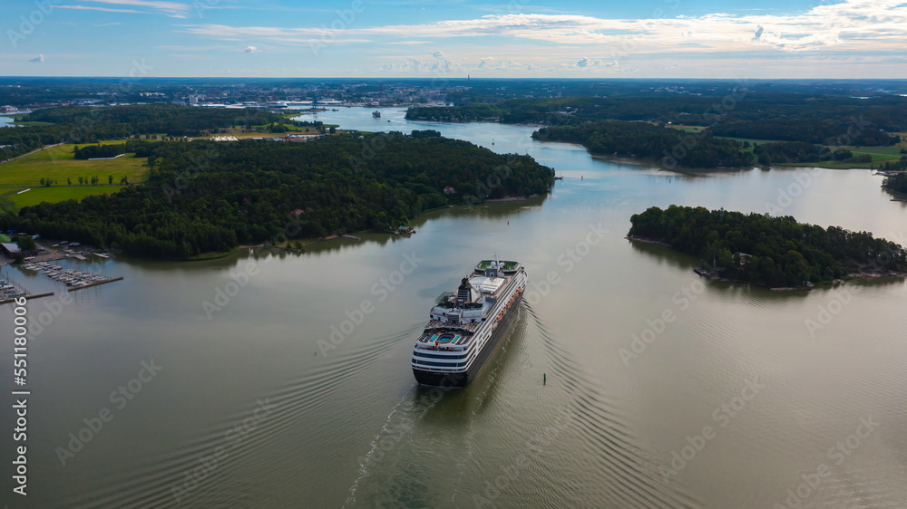Luxury cruise vessel making way ahead in beautiful Finnish archipelago. Narrow fairway and shoreline proximity. High altitude aerial stern view. Luxury cruise vessel making way ahead in beautiful Finnish archipelago. Narrow fairway and shoreline proximity. High altitude aerial stern view.