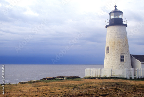 Early morning with overcast sky, deep blue horizon, and white stone tower of Pemaquid Point Light – a historic landmark located at tip of Pemaquid Neck in coastal Maine.