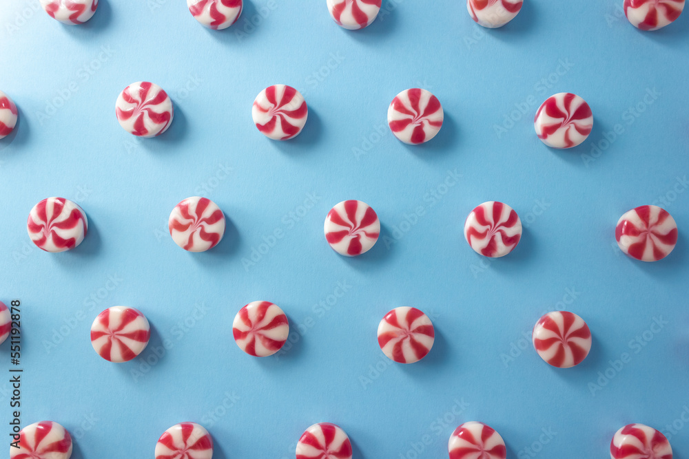 Fototapeta premium Christmas pattern of round striped caramel candies close-up on a blue background. Festive banner for confectionery. Selective focus.