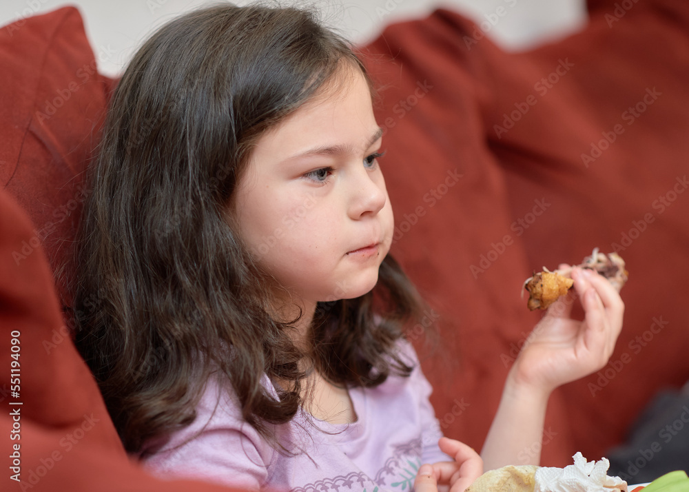 expressive young girl is eating chicken and vegetables for dinner on the couch while watching cartoons expressive young girl is eating chicken and vegetables for dinner on the couch while watching cartoons