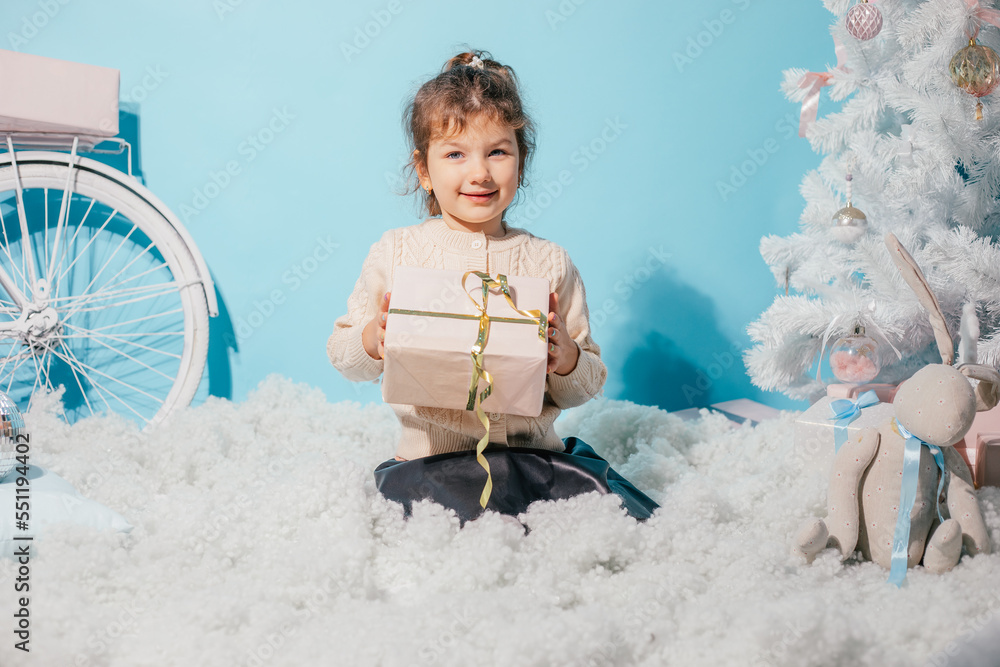 Naklejka premium Smiling merry, positive little girl getting surprise present box, sitting on soft cozy wadding carpet like cloud against