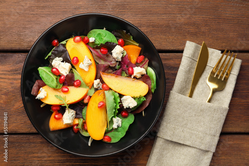 Delicious persimmon salad, knife and fork on wooden table, flat lay