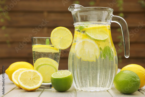 Water with lemons and limes on white wooden table outdoors