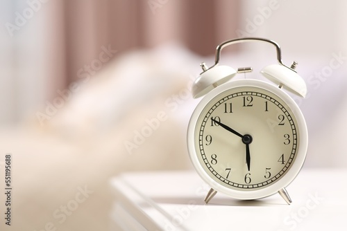 Stylish alarm clock on white nightstand indoors. Space for text