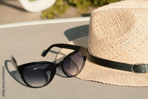 Stylish hat and sunglasses on grey sunbed outdoors, closeup