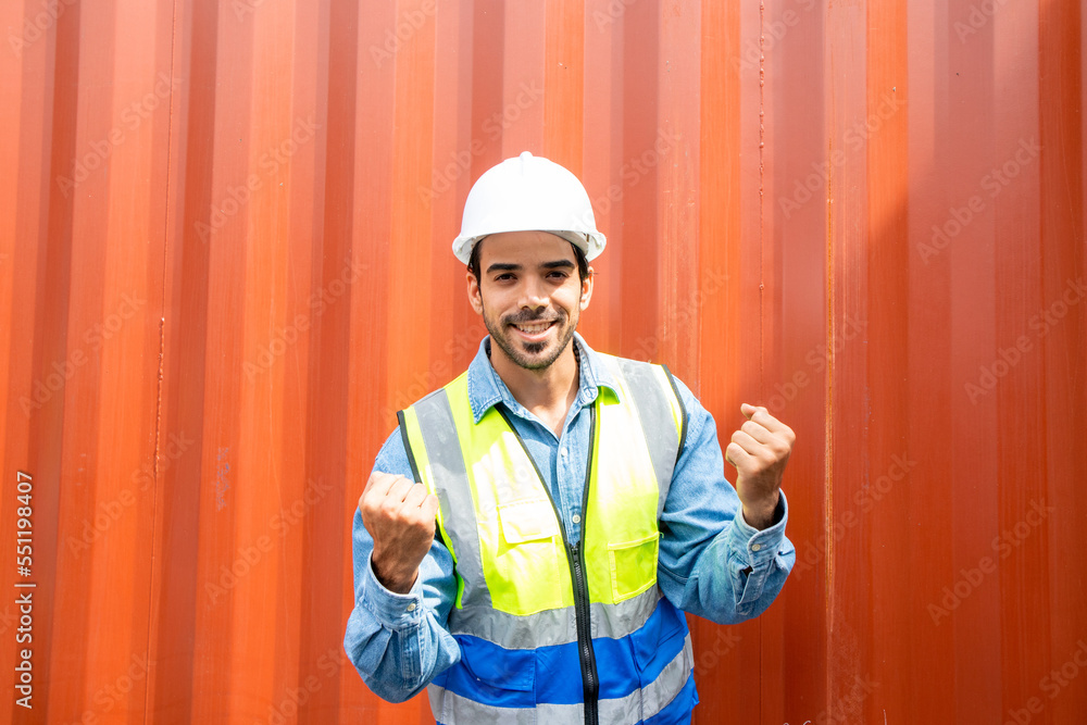 Portrait of successful young male engineer very happy and excited making winner gesture with arms up against container background. Portrait of successful young male engineer very happy and excited making winner gesture with arms up against container background.