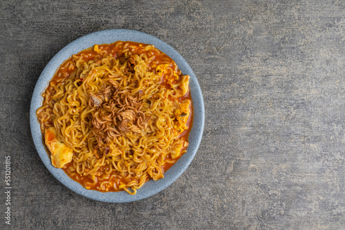 spicy fried instant noodle with egg and fried shallots on top on grey plate