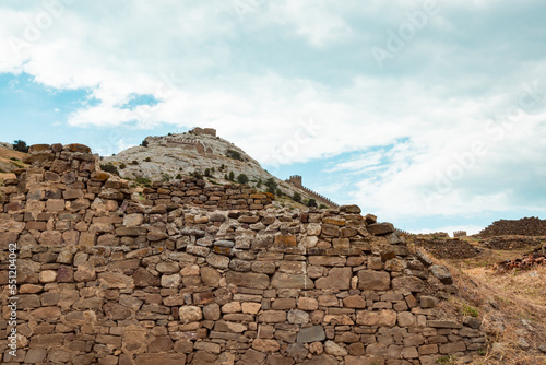 An old medieval wall and a mountain in the background. A large wall with a tower against a light blue sky.