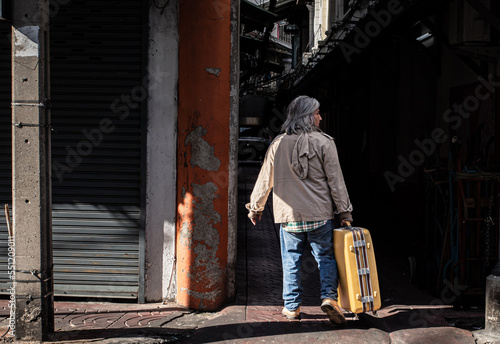 Tableau sur toile Asian homeless man dragging large suitcase in a narrow alley for to find rest, no home live on street, elderly man find new place sleep on sidewalk, health care problems for migrant refugees in slump