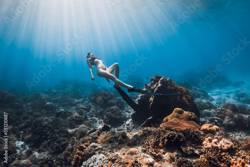 Woman freediver in bikini with fins glides on coral reef. Freediving in blue ocean with sun rays