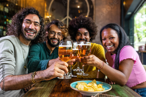Happy multiracial friends in a bar looking at camera toasting with beer.