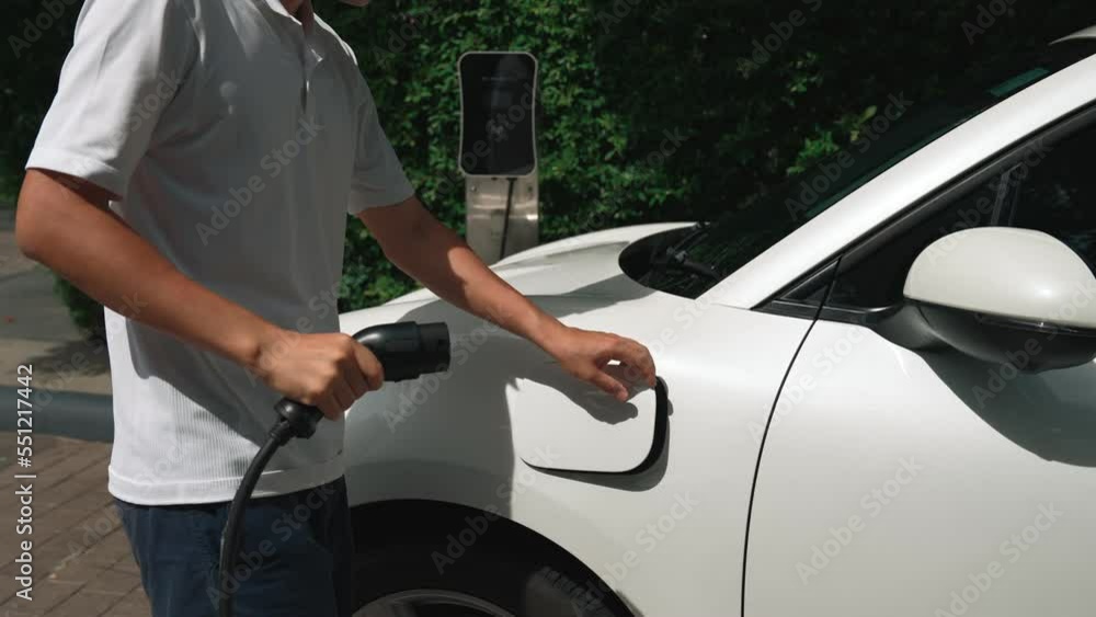 Progressive man install power cable plug to his electric vehicle, EV car from home charging