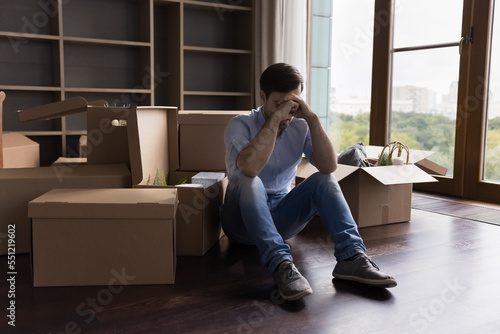 Tired unhappy bankrupt man moving out from apartment, sitting at pile of paper cardboard relocation boxes, waiting for delivery service, feeling headache, stress about eviction, divorce