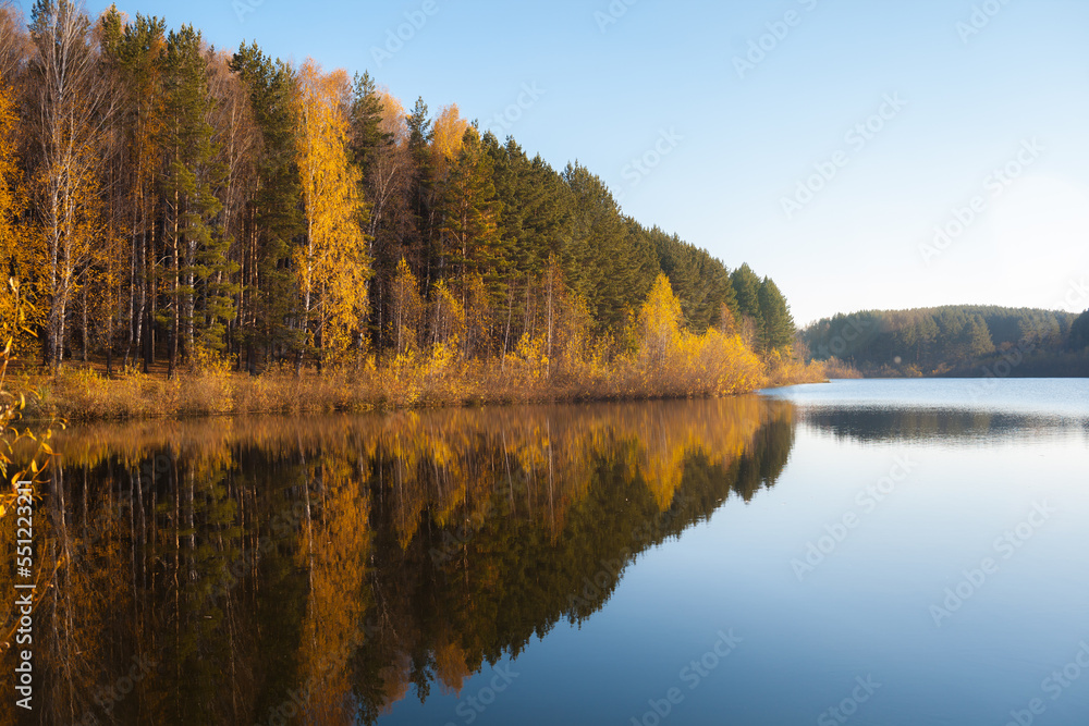 Colorful foliage tree reflections in calm pond water on a beautiful autumn day. A quiet and beautiful place to relax.