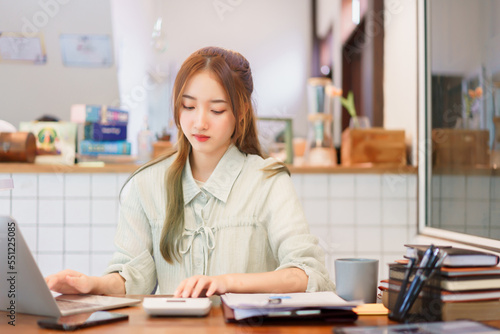 Coworking space office concept, Woman entrepreneur using calculator and typing data on laptop