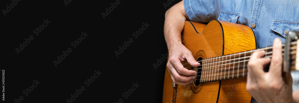 Obraz premium Guitarist playing acoustic guitar on black background, selective focus. A male musician plays the guitar. cover for online courses learning at home. A man playing guitar. Long wide banner, copy space