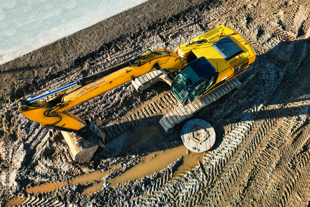 A powerful excavator digs the ground at a construction site. View from above. Drone photography. Earthworks with heavy equipment at the construction site.