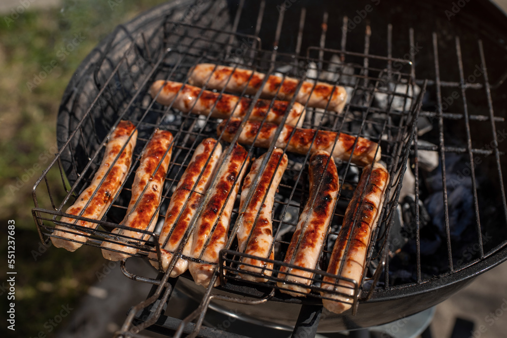 Closeup photo of sausages. Grilling chicken sausages outside on a barbecue grill. Grill tongs in the background. First outdoor grill party in the spring season. Healthy barbecue.