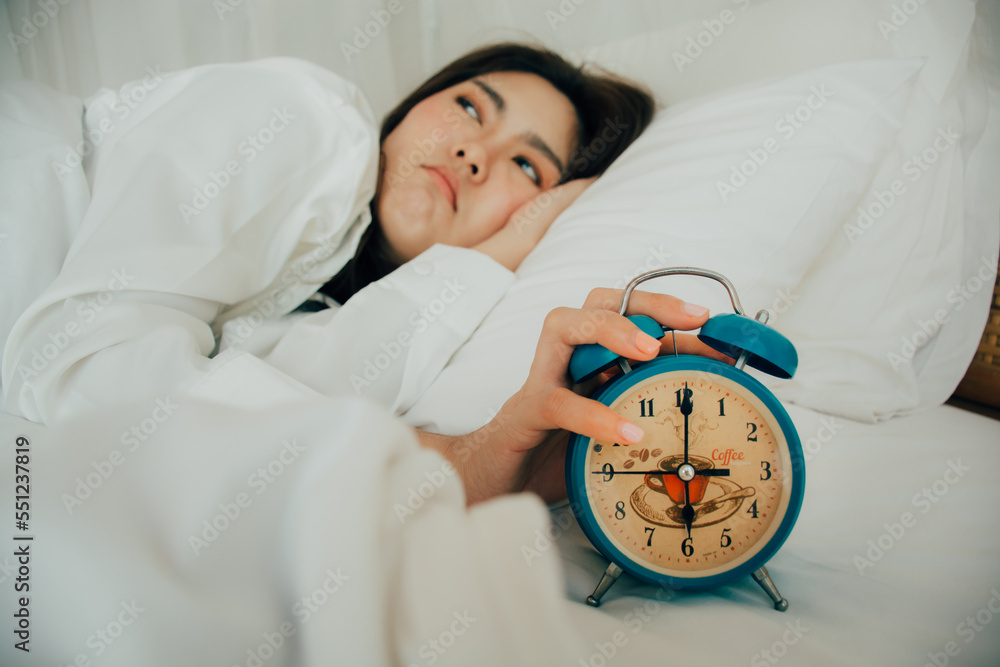 Asian beautiful woman in white pajamas turning off alarm clock while