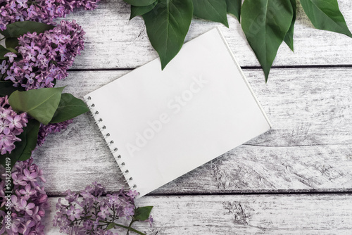 Spring layout. A notebook on a wooden background among lilac flowers. Morning, plans, mood