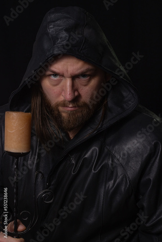 Portrait of a man in a cloak with a hood against a dark background with a candle on candlestick