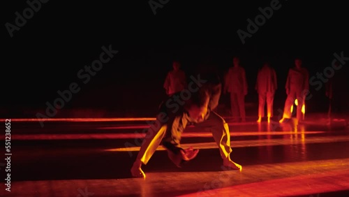 Silhouette of a female solo freestyler dancing barefoot on a dark stage with lights and smoke. Solo girl in modern dance on stage in orange light. A young hip hop dancer performs solo on stage in red photo